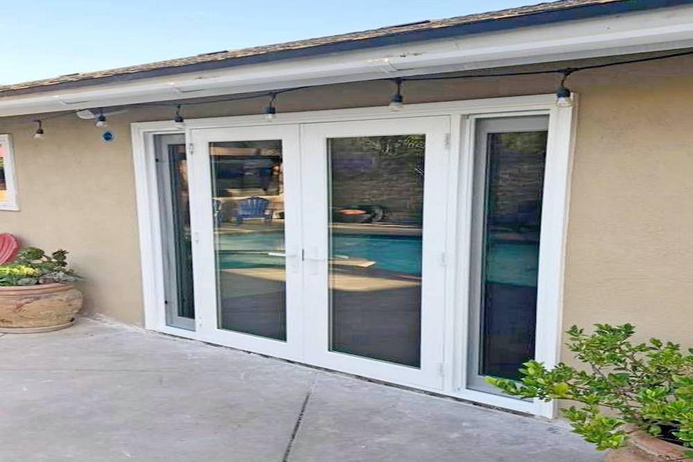 A set of sliding glass doors leading to a backyard with a pool, surrounded by potted plants